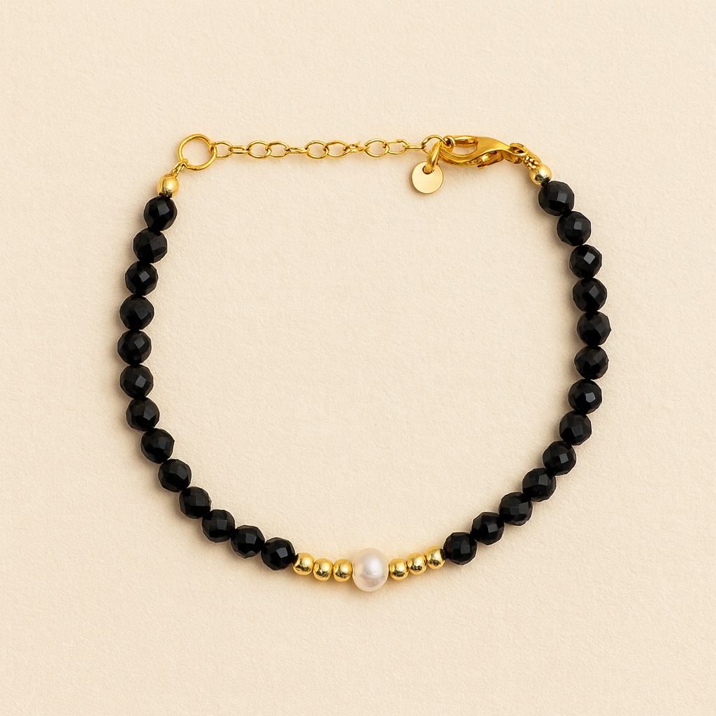 Bracelet with black beads, gold chain, and pearl on a beige background      